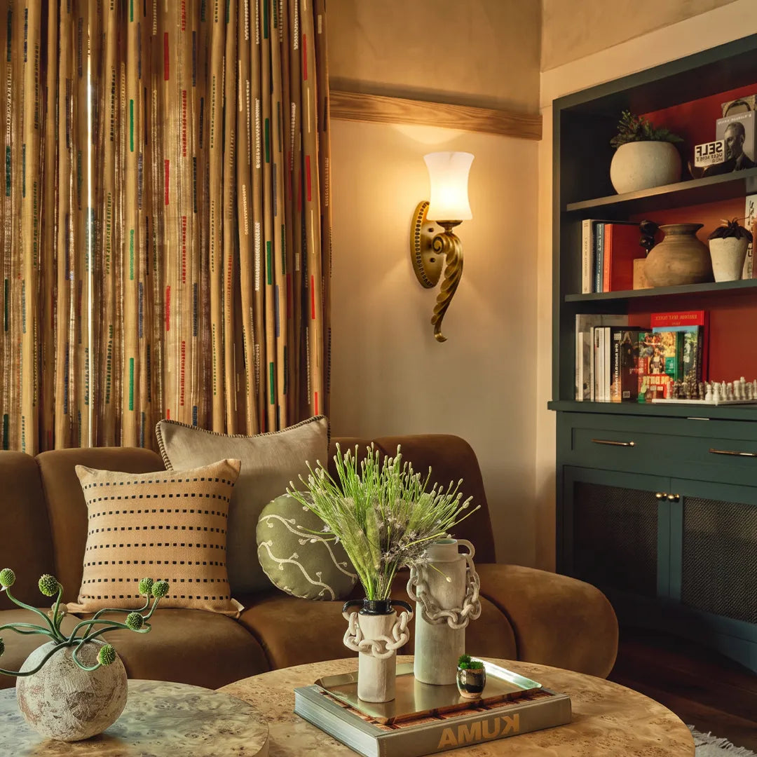 Vintage brass wall sconce illuminating a reading corner with striped wallpaper and warm accent light.