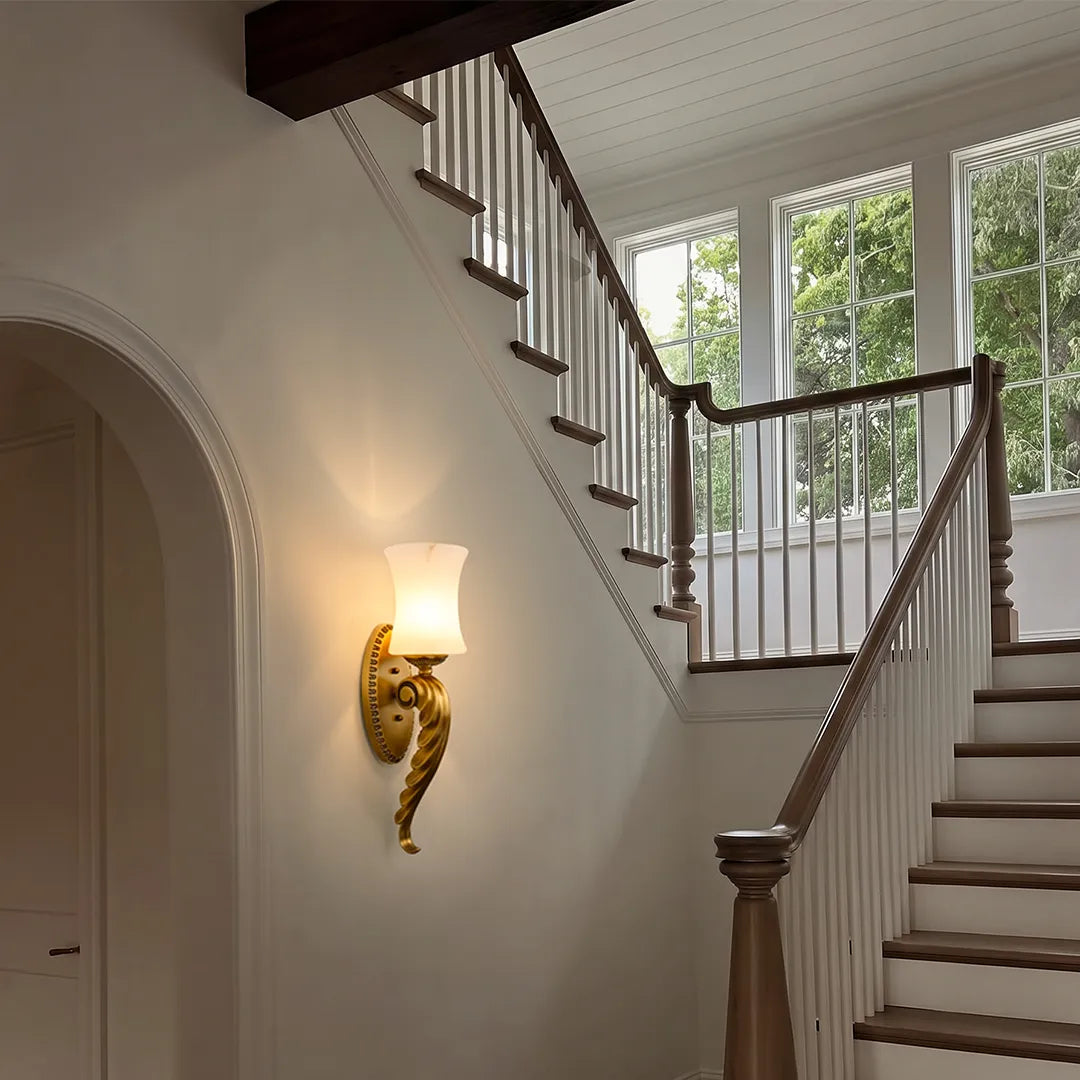 Vintage brass wall sconce mounted along a staircase wall with elegant curved detailing and warm light.