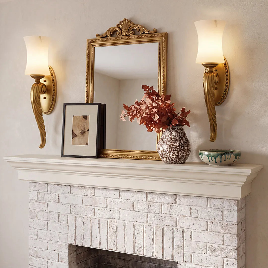 Vintage brass wall sconces installed above a white mantel with ornate mirror and soft warm lighting.