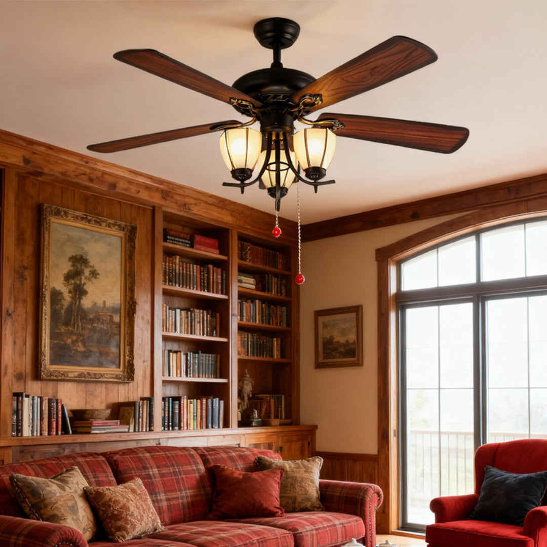 Vintage style ceiling fan with lights illuminating library room with built-in bookshelves and classic furniture.