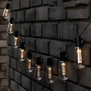 Solar camping string lights with vintage Edison bulb design creating warm ambient lighting along brick wall for outdoor gatherings
