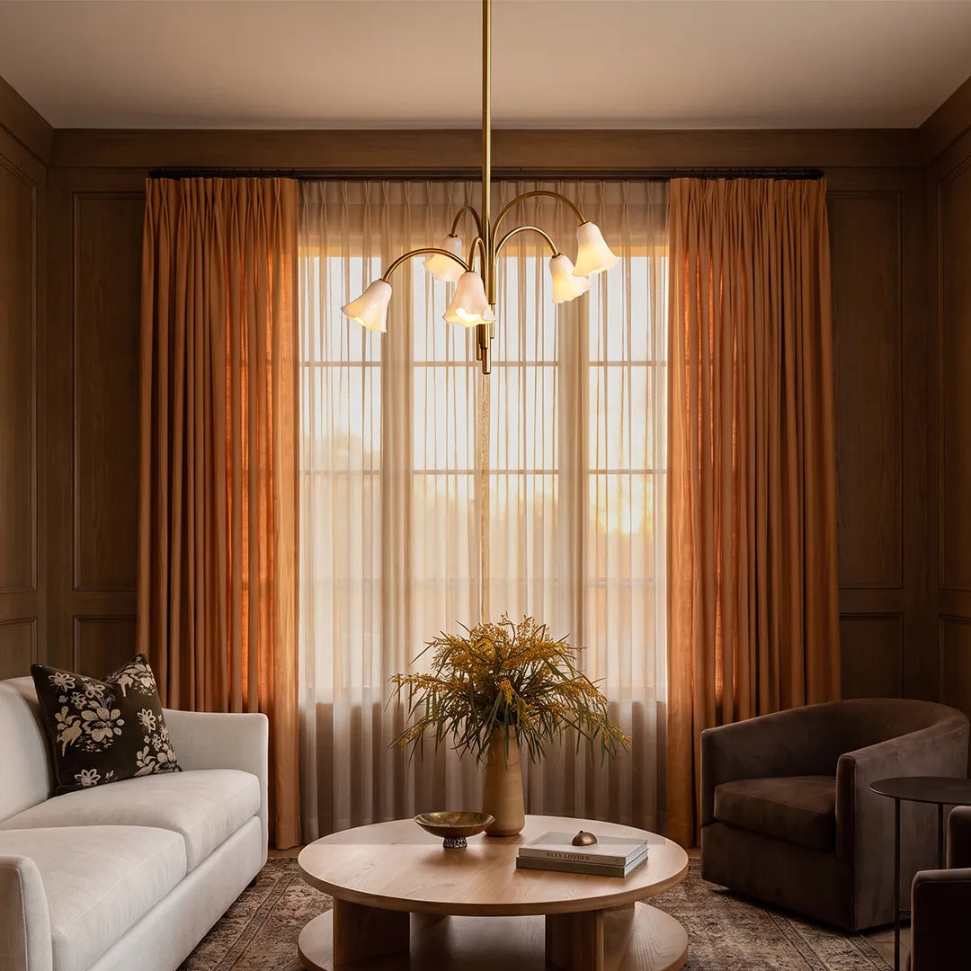 Vintage flower chandelier installed in a warm living room with wood-paneled walls, soft drapery, and elegant seating.
