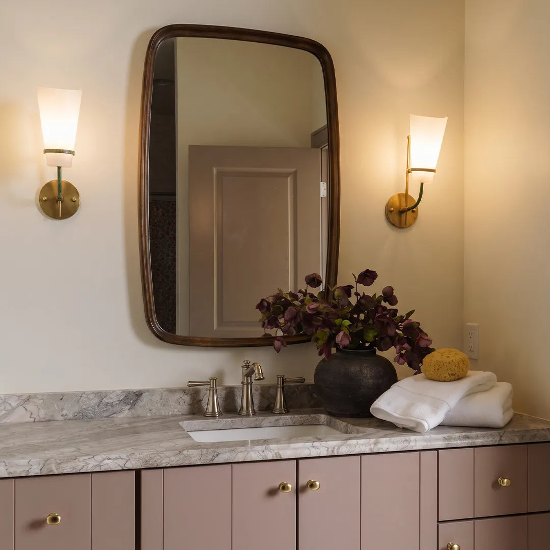 Vintage French wall lights installed beside a bathroom mirror with a warm brass finish and frosted glass shade.