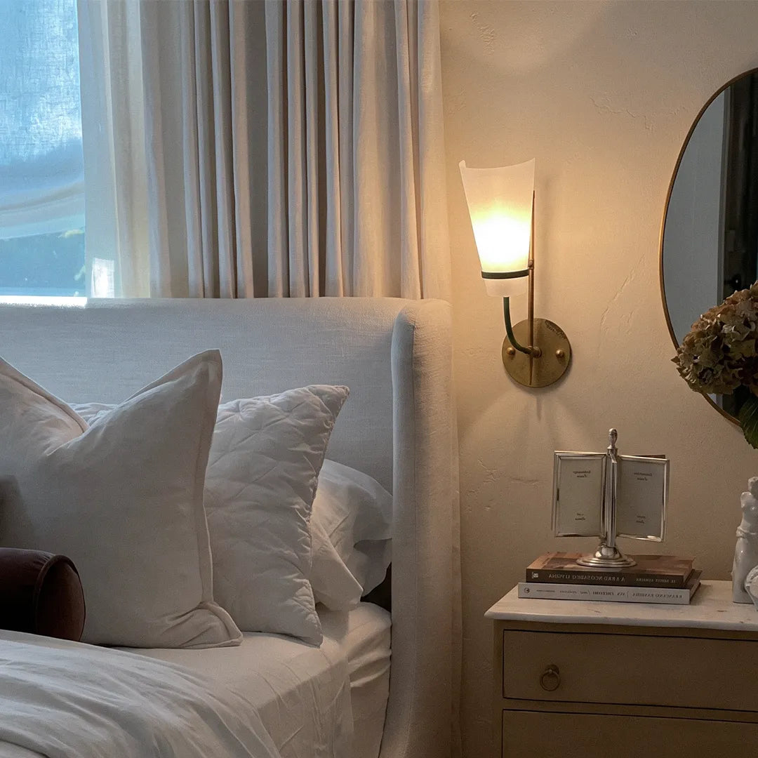 Vintage French wall lights placed beside a bed with a frosted glass shade and antique brass wall mount.