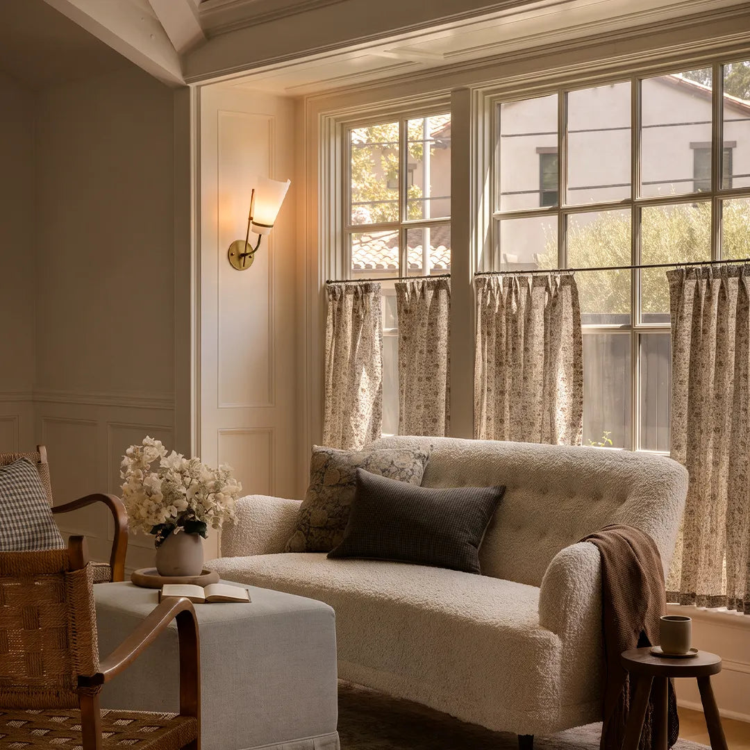 Vintage French wall lights illuminating a cozy sitting room with a sofa, window, and warm classic styling.