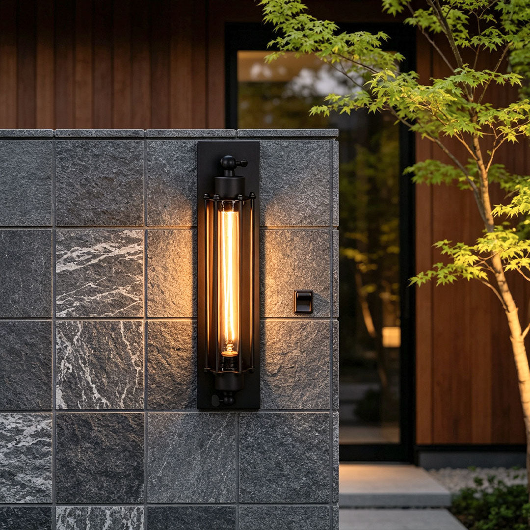 Vintage industrial wall sconce mounted on a dark stone wall near a modern entry with warm vertical illumination.