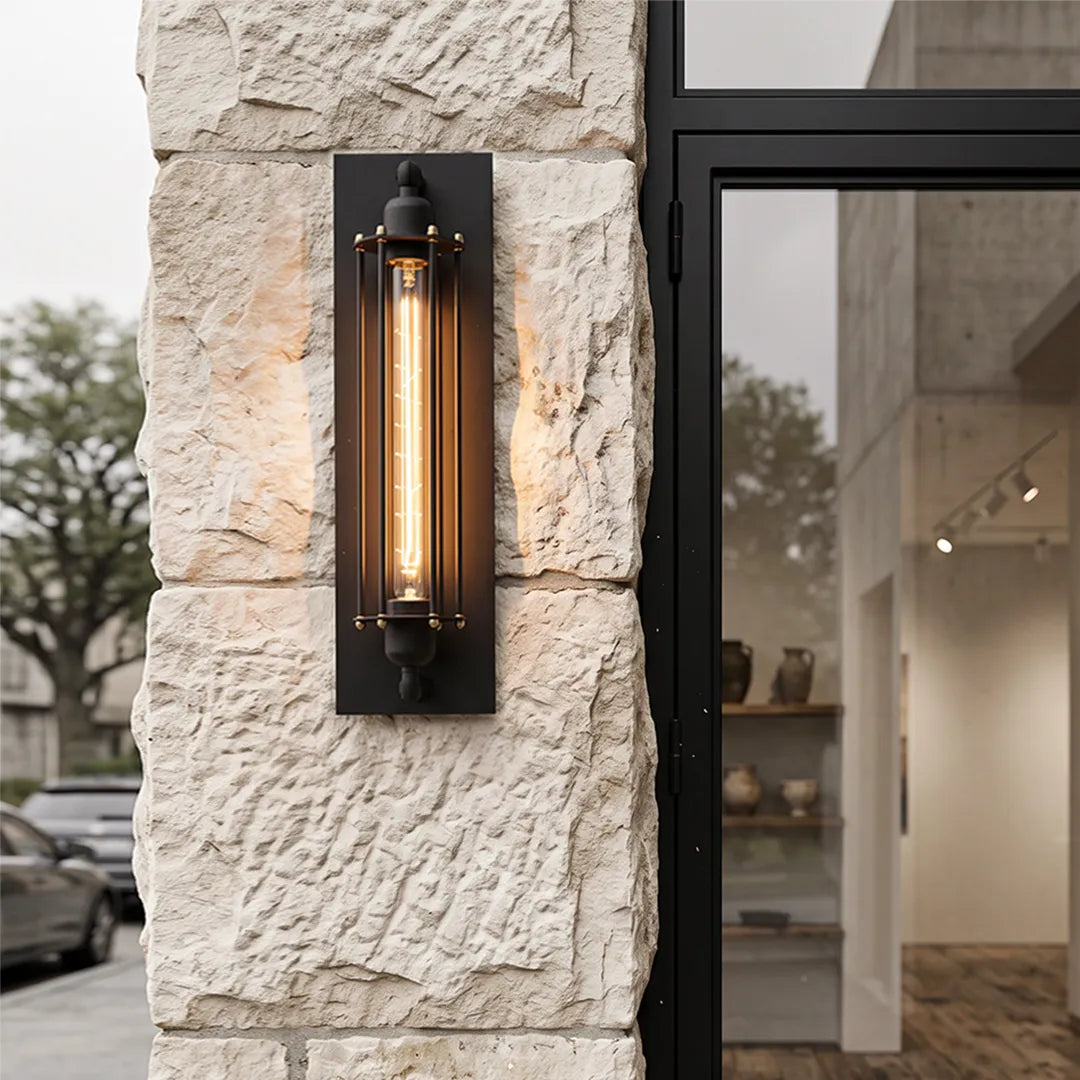 Vintage industrial wall sconce mounted on a textured stone exterior wall beside a modern glass door.