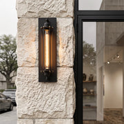 Vintage industrial wall sconce mounted on a textured stone exterior wall beside a modern glass door.