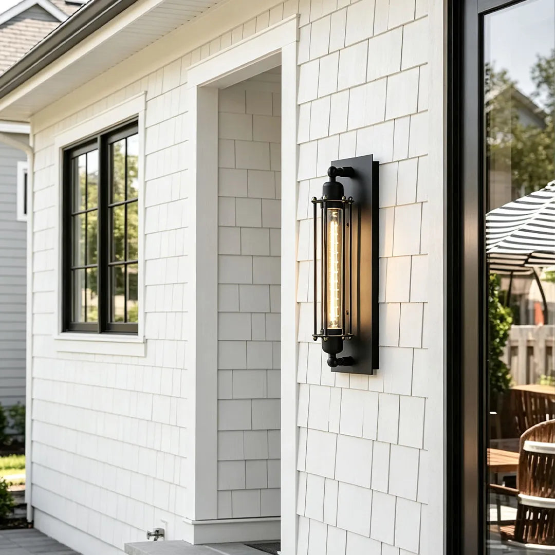 Vintage industrial wall sconce installed on white exterior siding beside a black framed window.