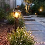 Vintage outdoor bollard light with warm glow beside stone garden pathway