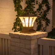 Vintage outdoor pillar lantern with warm glow on brick column beside garden plants