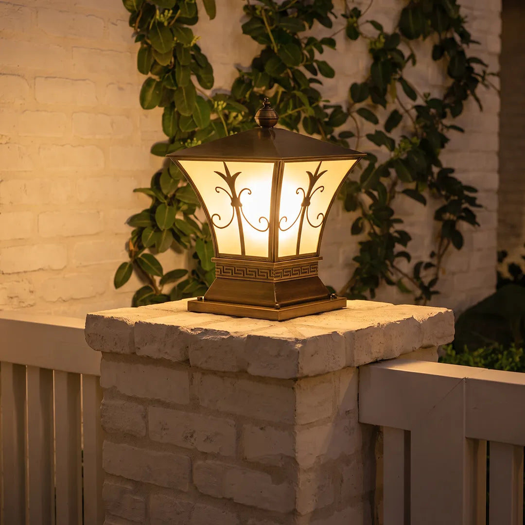 Vintage outdoor pillar lantern with warm glow on brick column beside garden plants