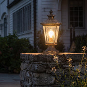 Vintage outdoor pillar lantern with warm glow on stone column beside garden
