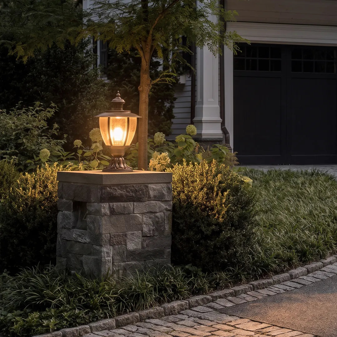 Vintage outdoor pillar light with warm glow on stone column beside garden