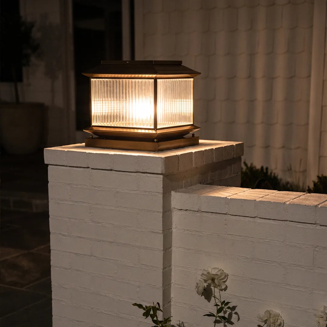Vintage outdoor pillar light with warm glow on white brick column beside home