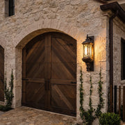 Vintage outdoor wall lantern mounted beside an arched wood entry door on a stone exterior wall.