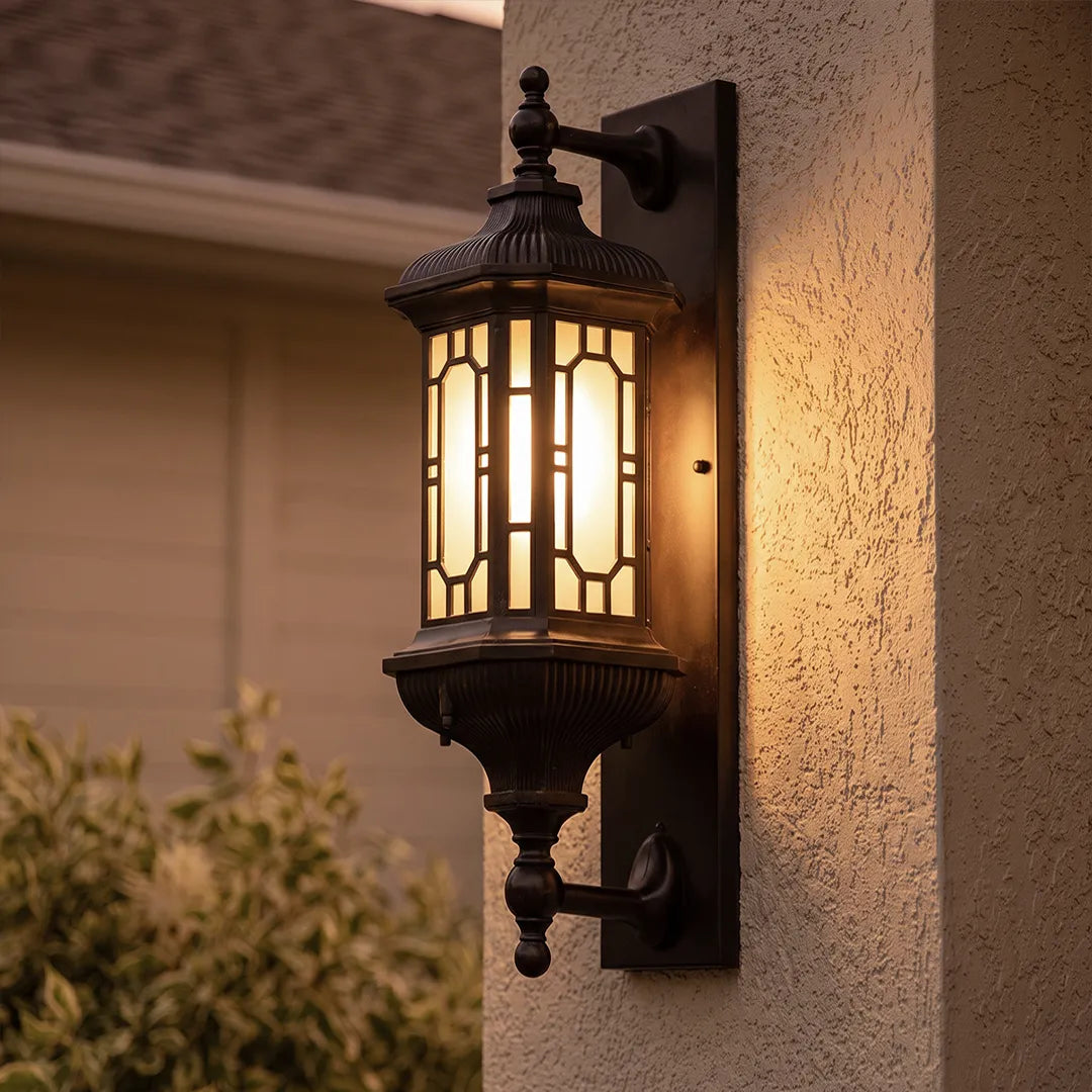 Close-up of a vintage outdoor wall lantern with warm light mounted on a textured stucco wall.