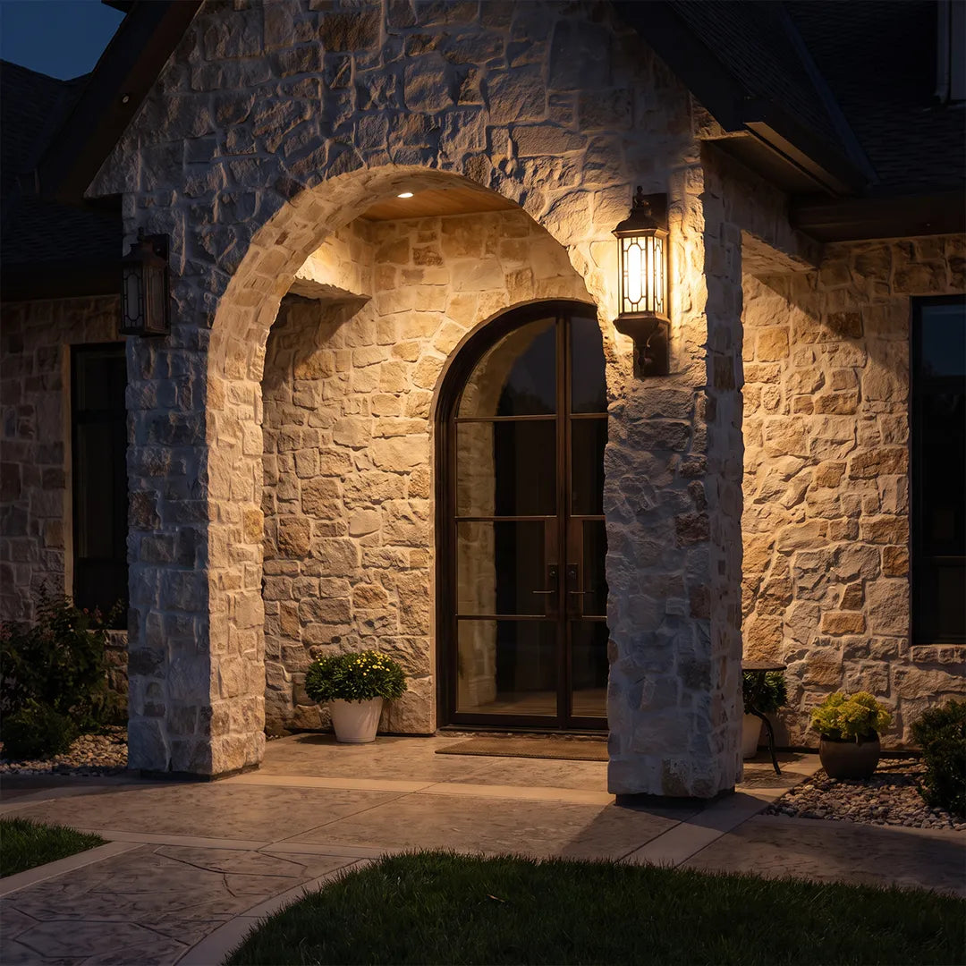 Vintage outdoor wall lanterns illuminating a stone home entryway with arched columns at dusk.