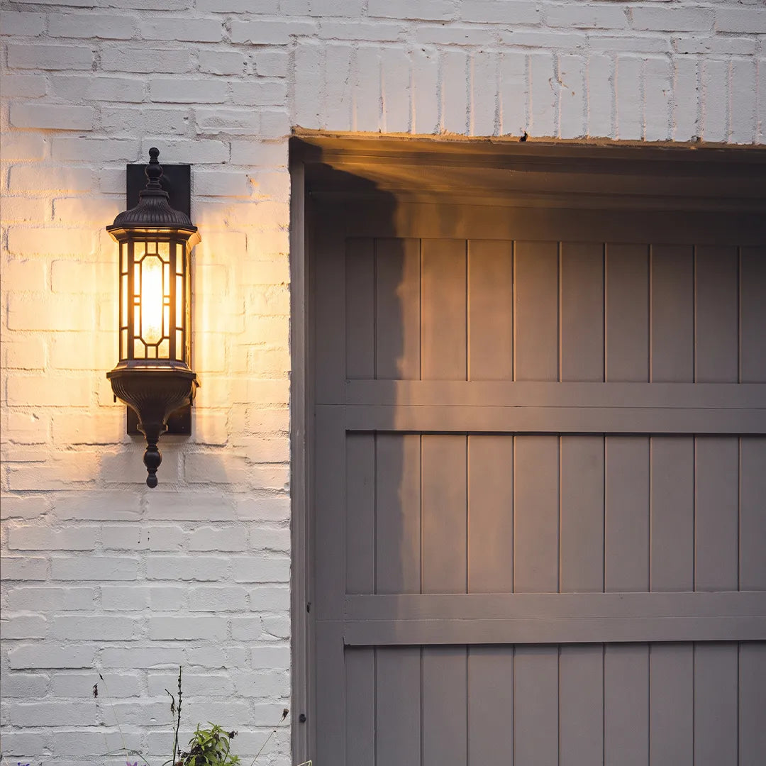 Vintage outdoor wall lantern mounted on a white brick wall beside a gray garage-style exterior door.