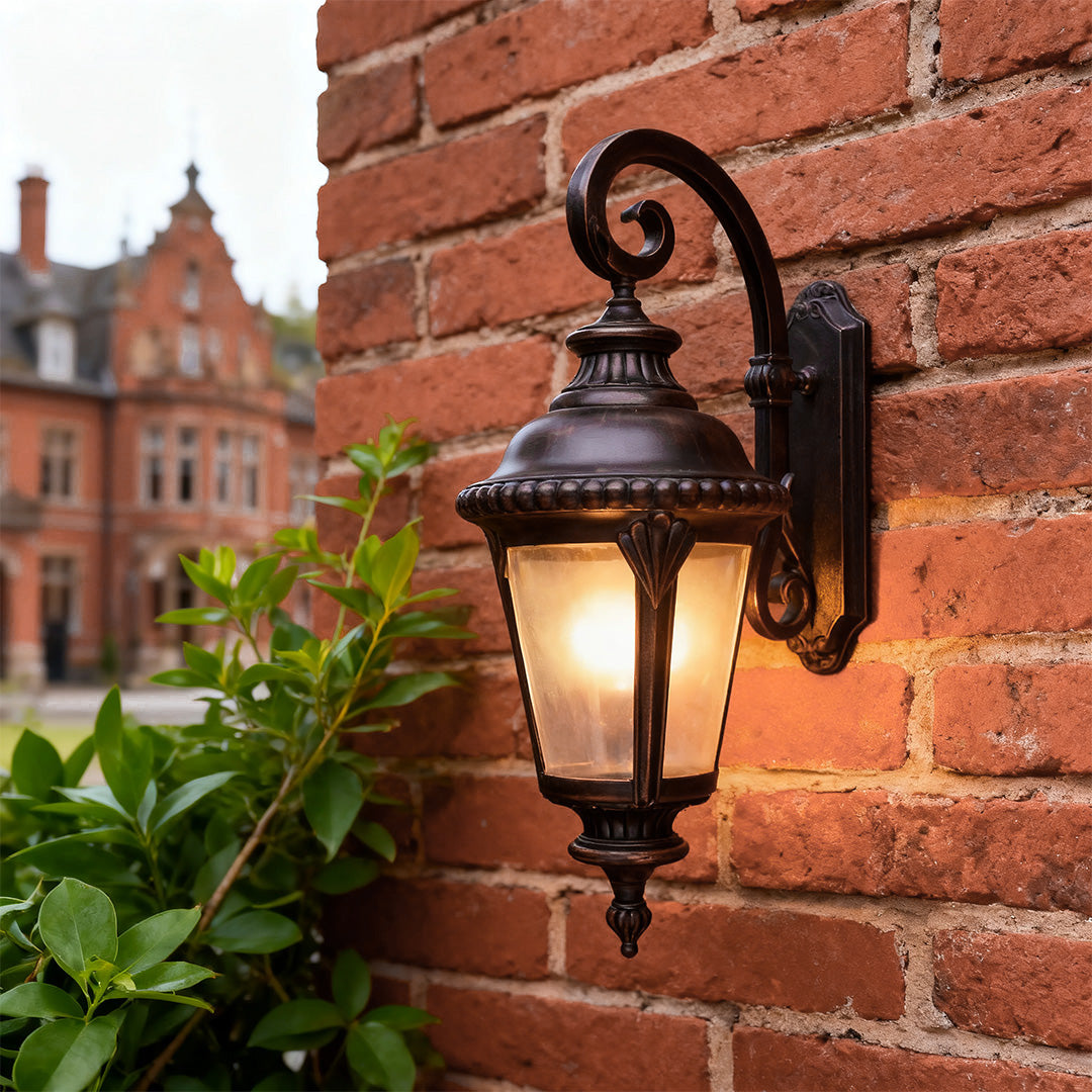 Vintage outdoor wall sconce casting warm glow on red brick wall near green plant foliage