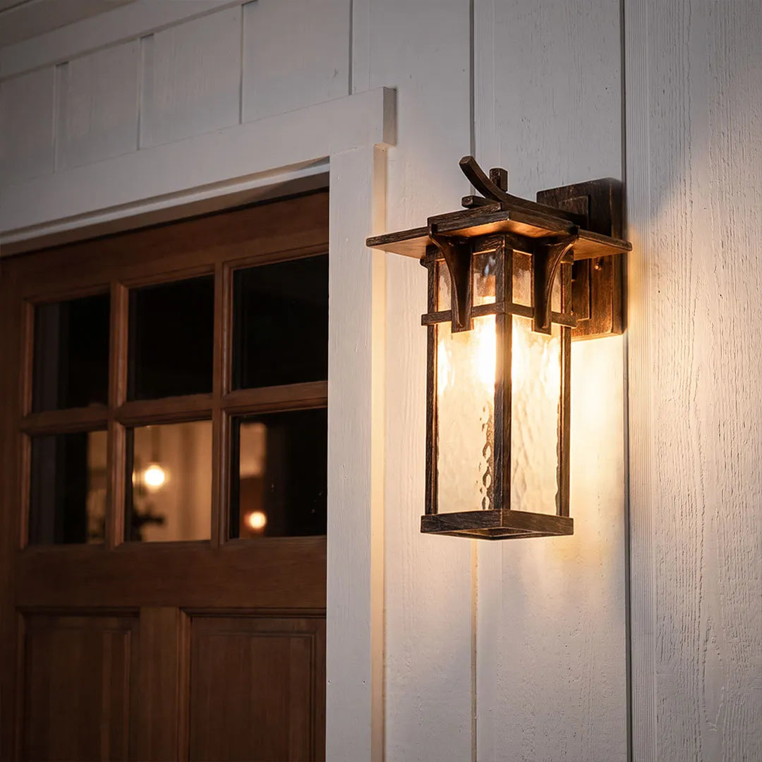 Vintage sconce wall light glowing beside an entryway with an ornate bronze backplate and curved arm.