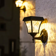 Vintage-style solar outdoor sconce lights with textured glass casting a warm, patterned glow on a concrete wall.