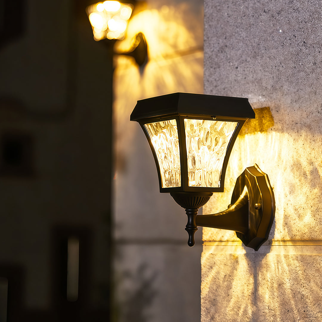 Vintage-style solar outdoor sconce lights with textured glass casting a warm, patterned glow on a concrete wall.