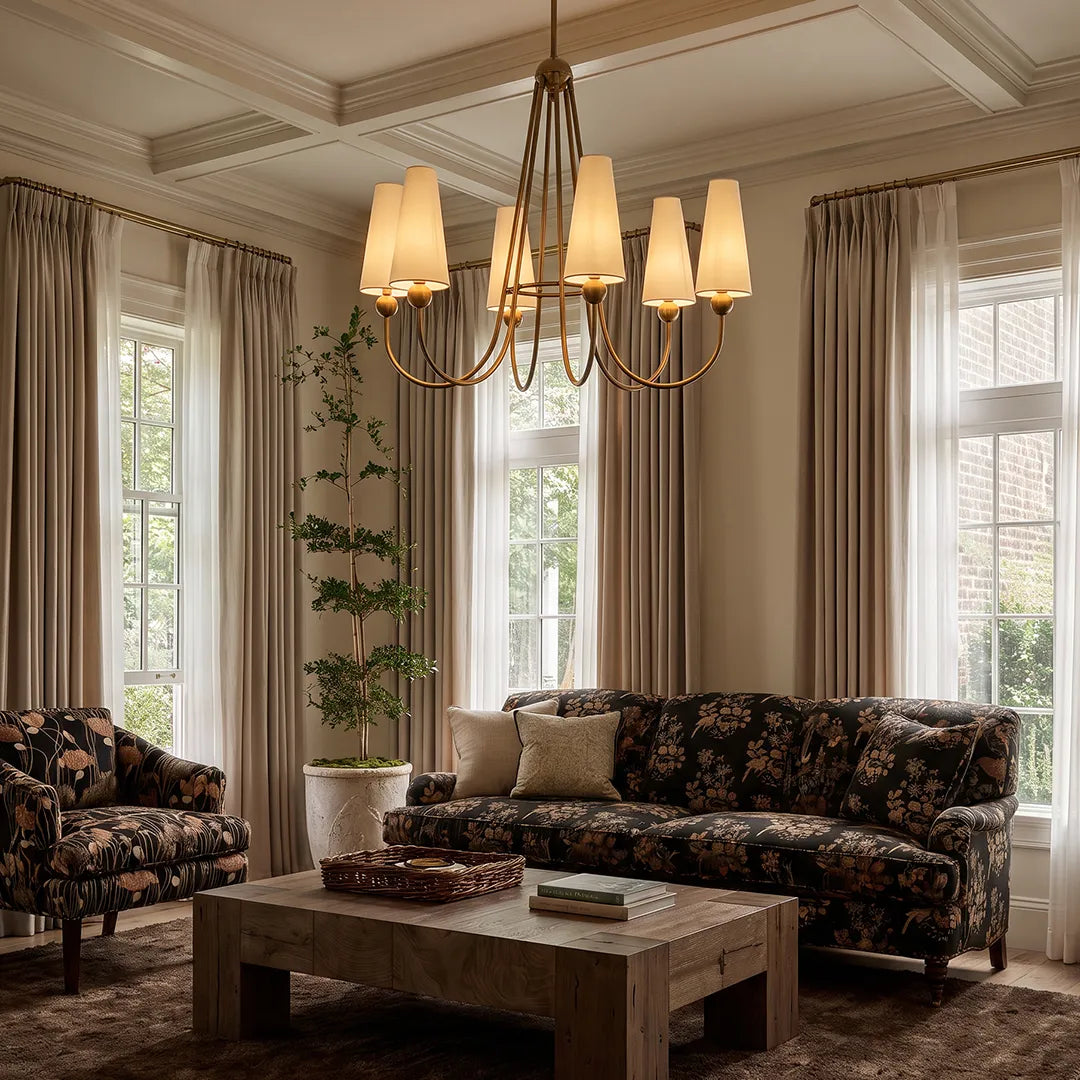 Vintage solid brass chandelier installed in an elegant living room with floral seating and tall sunlit windows.
