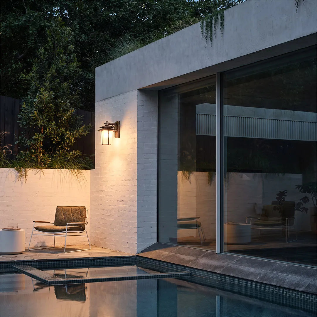 Vintage wall sconce light fixtures illuminating a modern outdoor patio beside large glass doors.