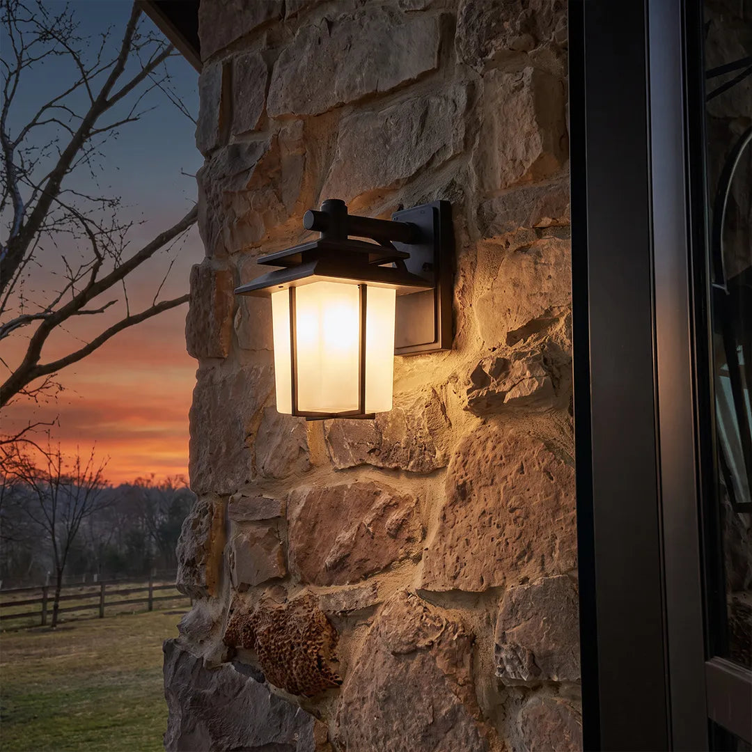 Vintage wall sconce light fixtures glowing warmly against a rustic stone wall at dusk.