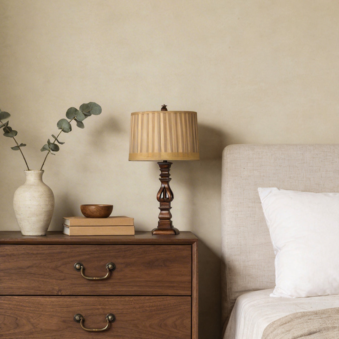 Vintage wood table lamp with a beige shade, placed on a wooden nightstand in a cozy bedroom.
