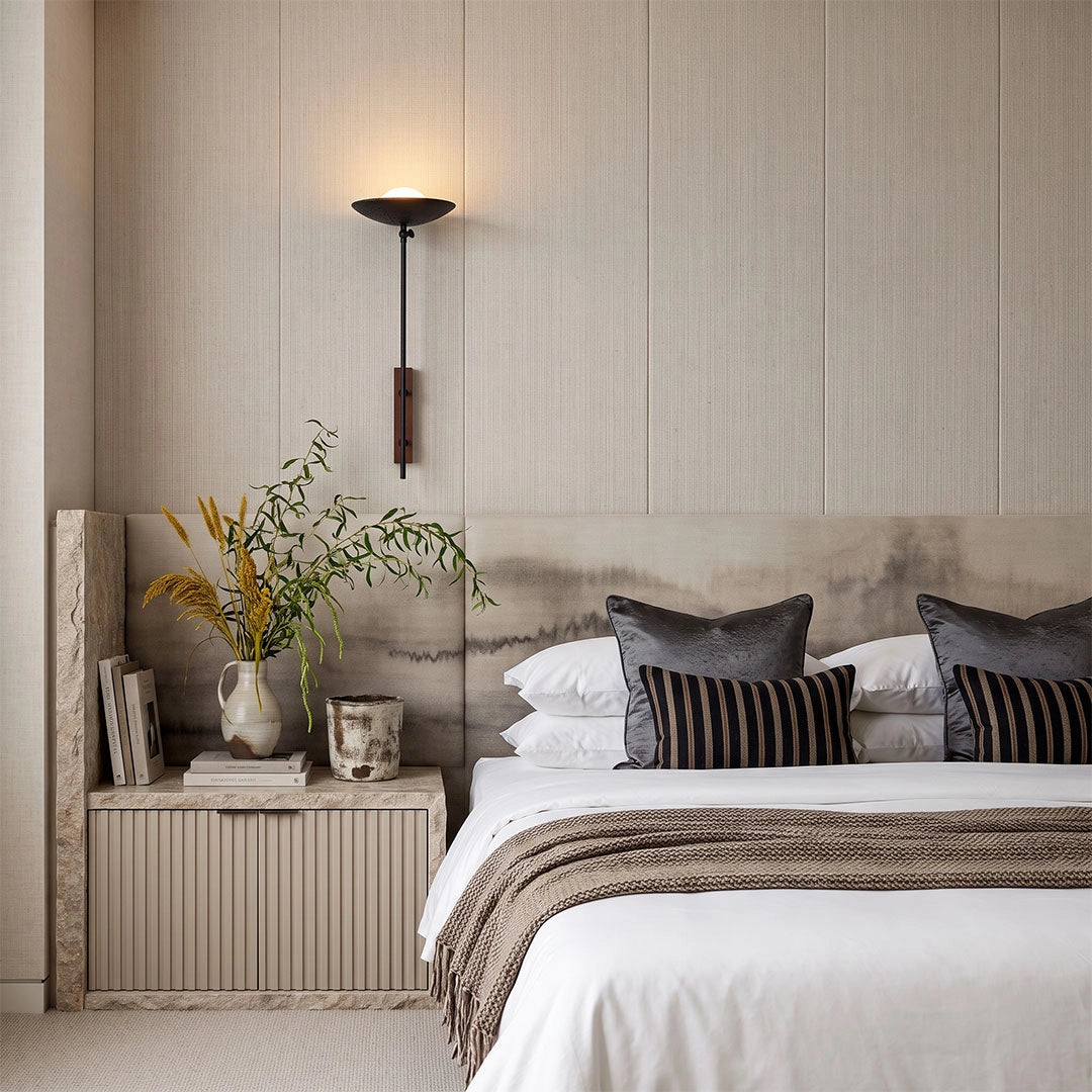 Wall adjustable light installed beside a bed with a long vertical arm and wide disc-shaped shade.