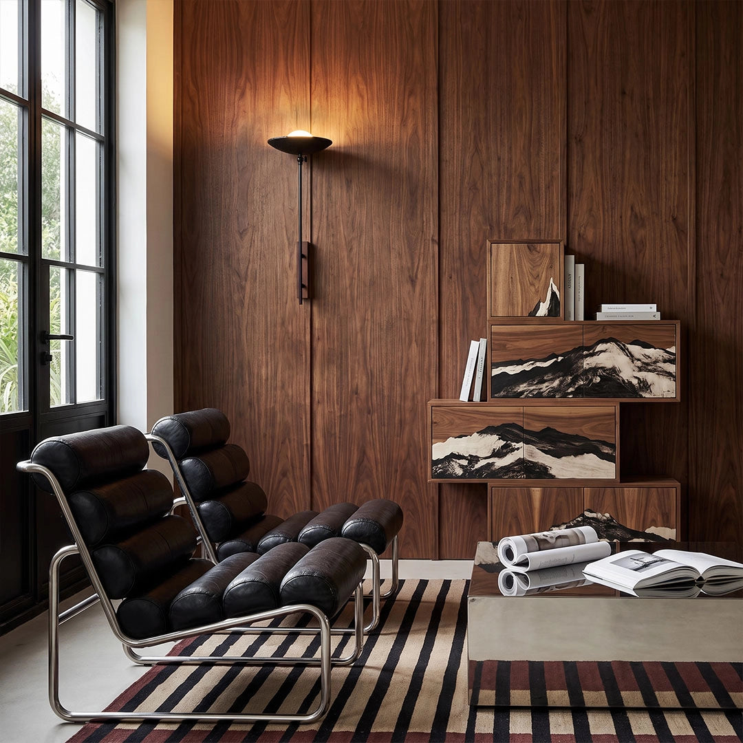 Wall adjustable light mounted on a dark wood wall beside black lounge chairs in a contemporary interior.
