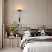 Wall adjustable light mounted beside a bed in a warm neutral bedroom with layered bedding.