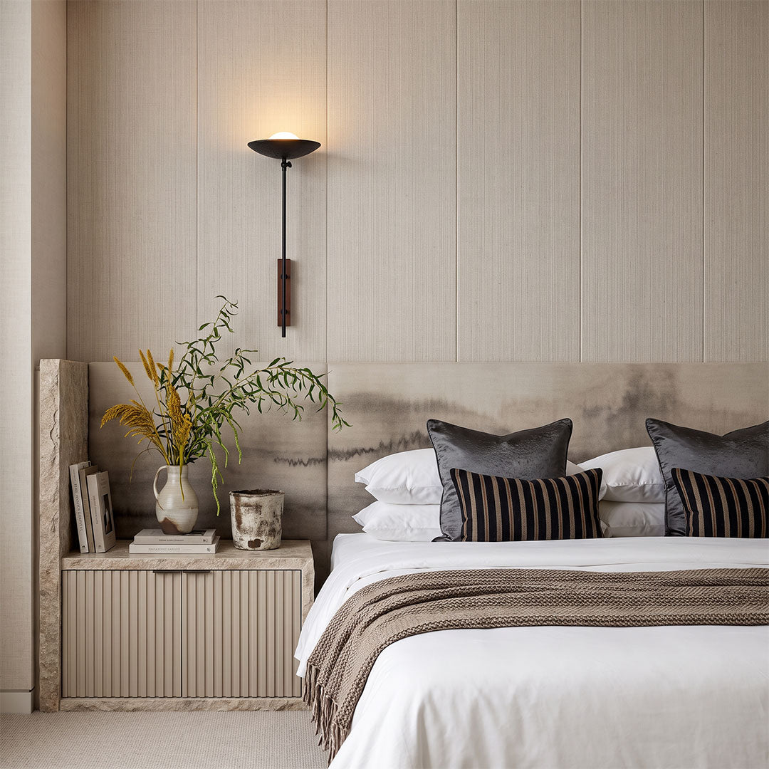 Wall adjustable light mounted beside a bed in a warm neutral bedroom with layered bedding.