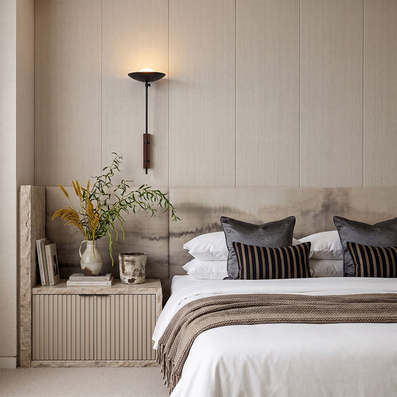 Wall adjustable light mounted beside a bed in a warm neutral bedroom with layered bedding.