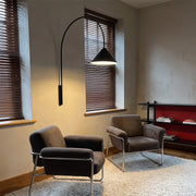 Wall arm light with a long curved black arm and cone-shaped shade mounted beside a window in a modern sitting area.