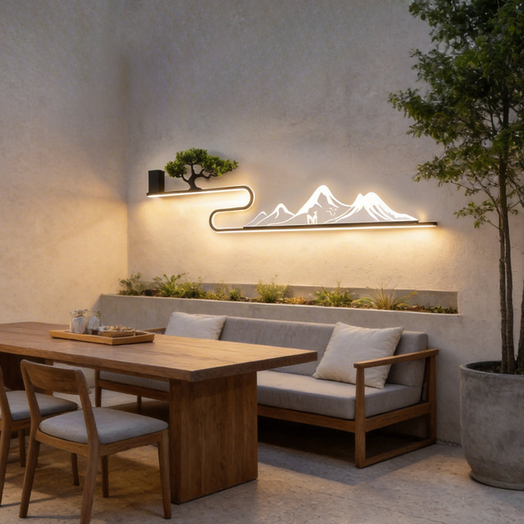 Wall art with light in a garden setting, featuring a mountain silhouette and bonsai tree.