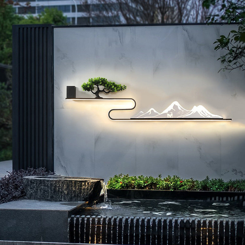 Wall art with light in a modern outdoor space, featuring a mountain silhouette and tree.