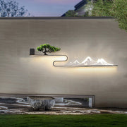 Wall art with light featuring a mountain and tree silhouette, installed on an outdoor wall.