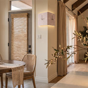 Wall clock lamp mounted in an entryway corner, casting soft light near a doorway and woven chair.