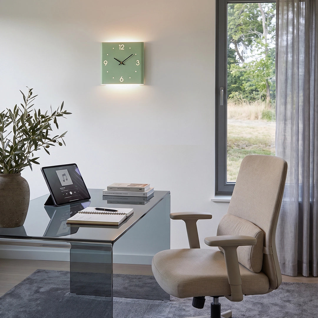 Wall clock lamp glowing above a desk in a bright home office with a chair and window view.