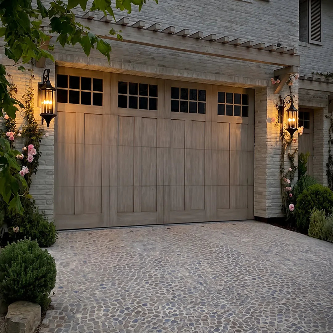 Wall lanterns outdoor lighting mounted on both sides of a carriage-style garage door on a stone home exterior.