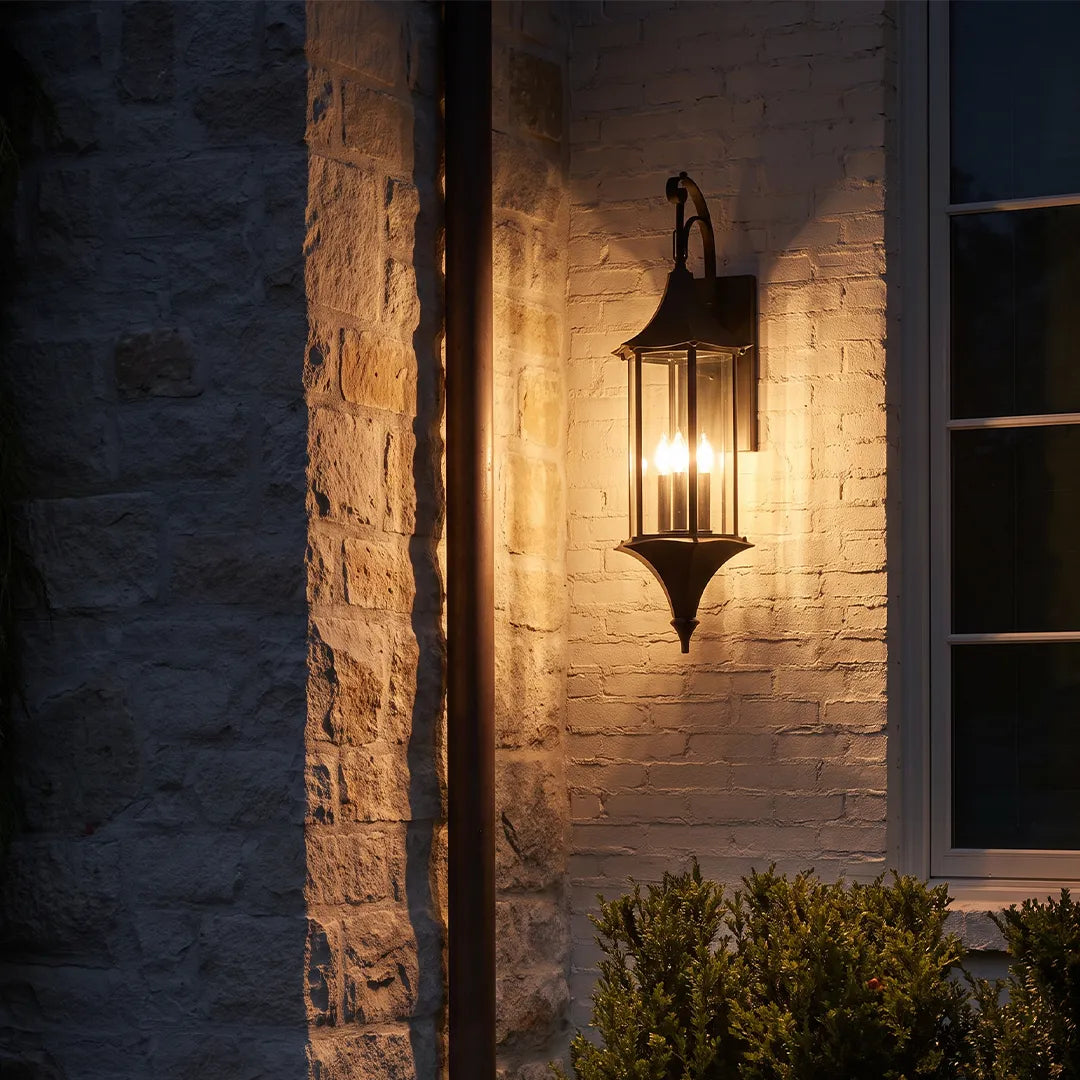 Wall lanterns outdoor lighting glowing at night on a brick wall beside a window and landscaped entryway.