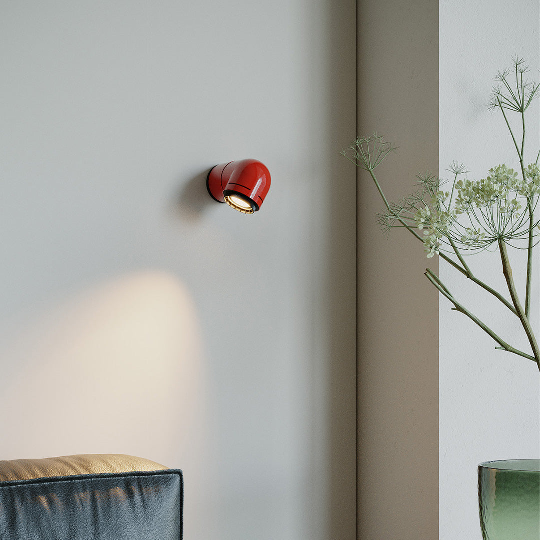 Red wall modern light illuminating a soft neutral wall in a cozy bedroom corner.