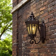 Wall mount light outdoor brightening rustic brick facade with ornate scroll bracket in daylight