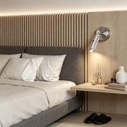 Modern wall mount reading light installed beside bed with brushed metal finish and warm LED illumination.