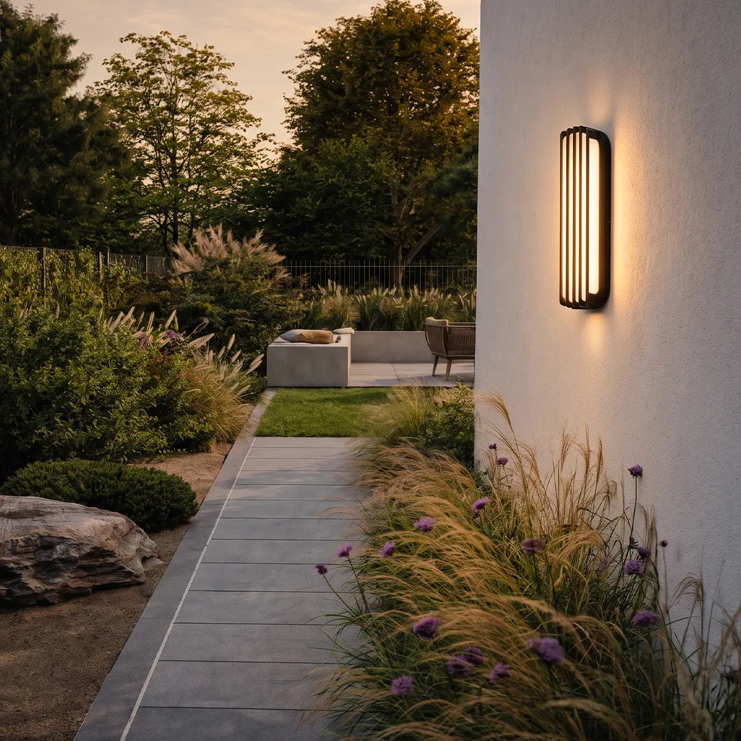Wall-mounted linear lighting mounted on a white exterior wall beside a garden path at dusk.