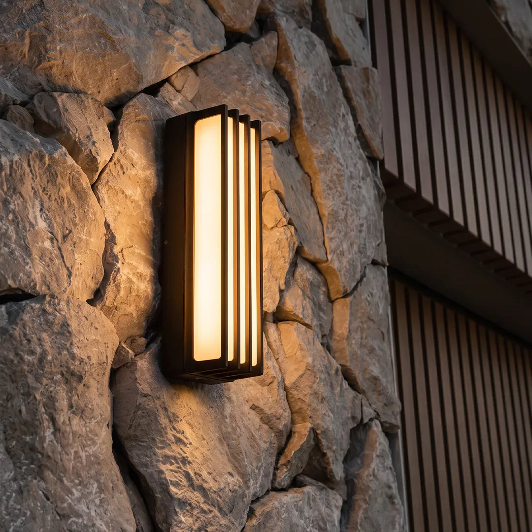 Wall-mounted linear lighting installed on a stone wall, casting a warm glow on a modern exterior.