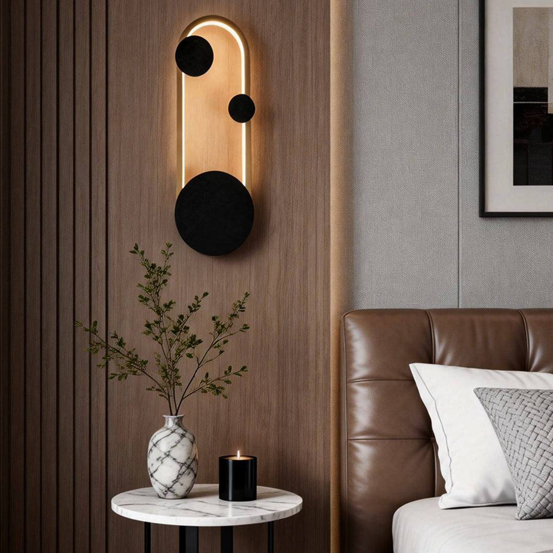 Wall mounted nightstand lights featuring a gold frame and black discs, enhancing a cozy modern bedroom corner.